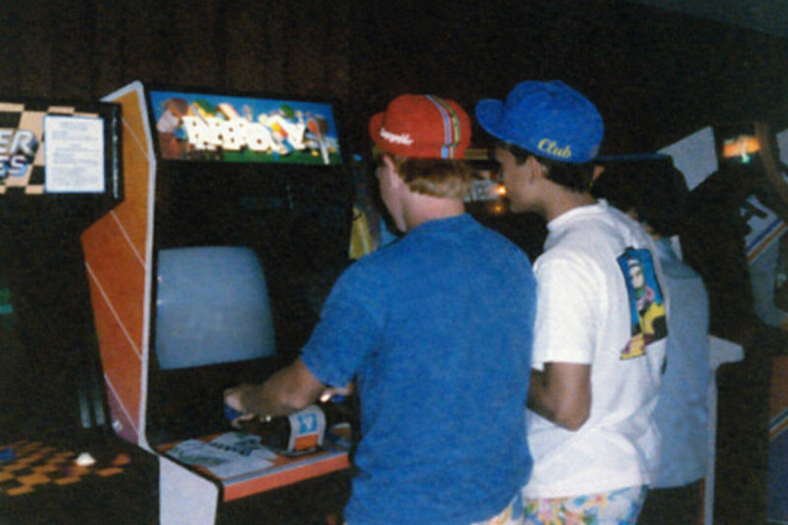 Jugadores con gorras de los 90 en una máquina arcade Paperboy Boy