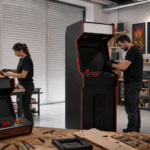 Taller profesional de fabricación de máquinas arcade y bartop en España, con trabajador y trabajadora ensamblando muebles recreativos, arcades completos y pósters de videojuegos clásicos retro.