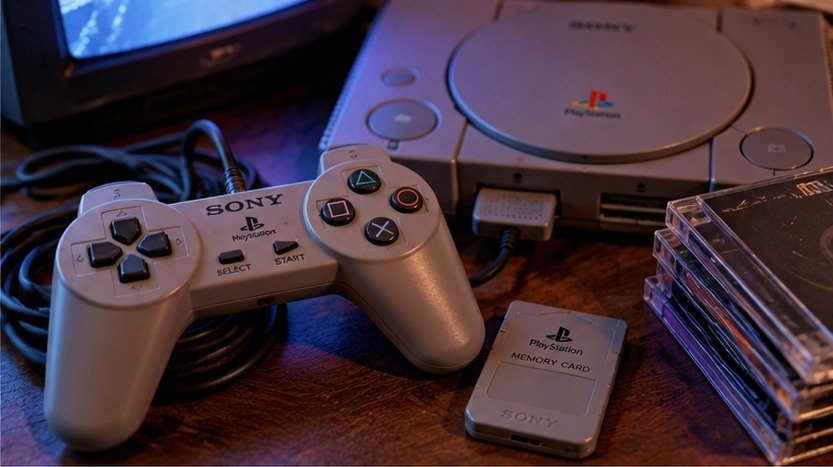 Mando gris y memory card junto a una consola PlayStation 1 y cajas de juegos